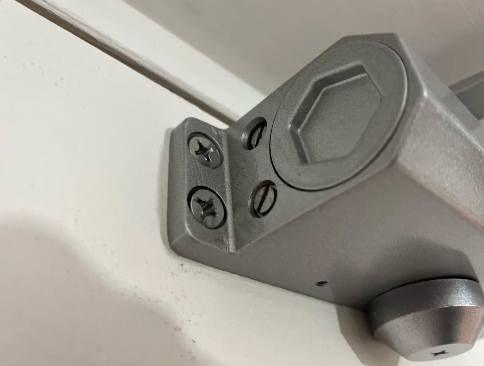 Commercial door closer showing oil leak stain on arm and bracket indicating internal seal failure